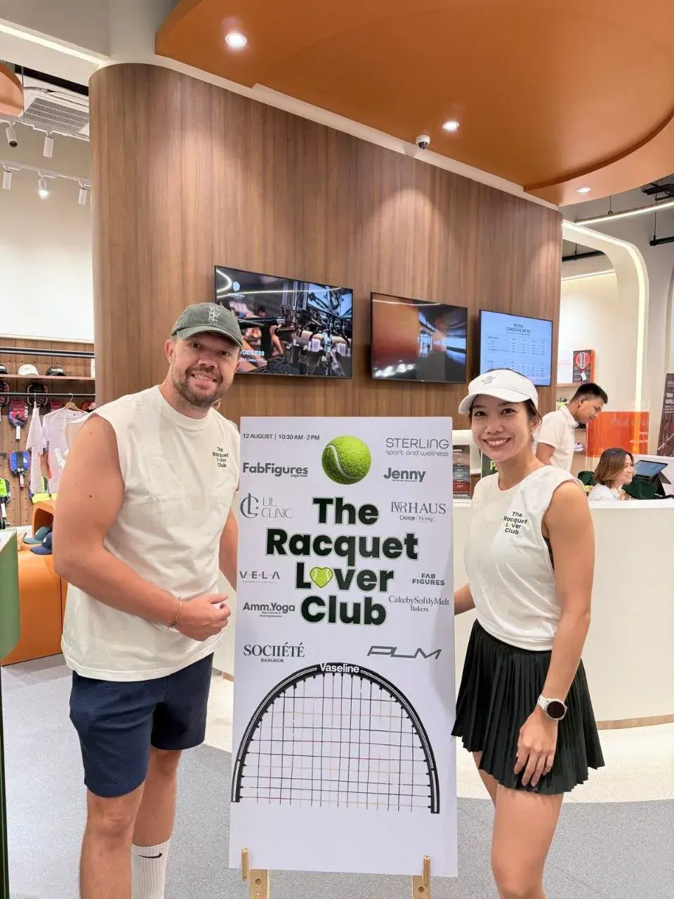 Two guests beside the Racquet Lovers Club event board